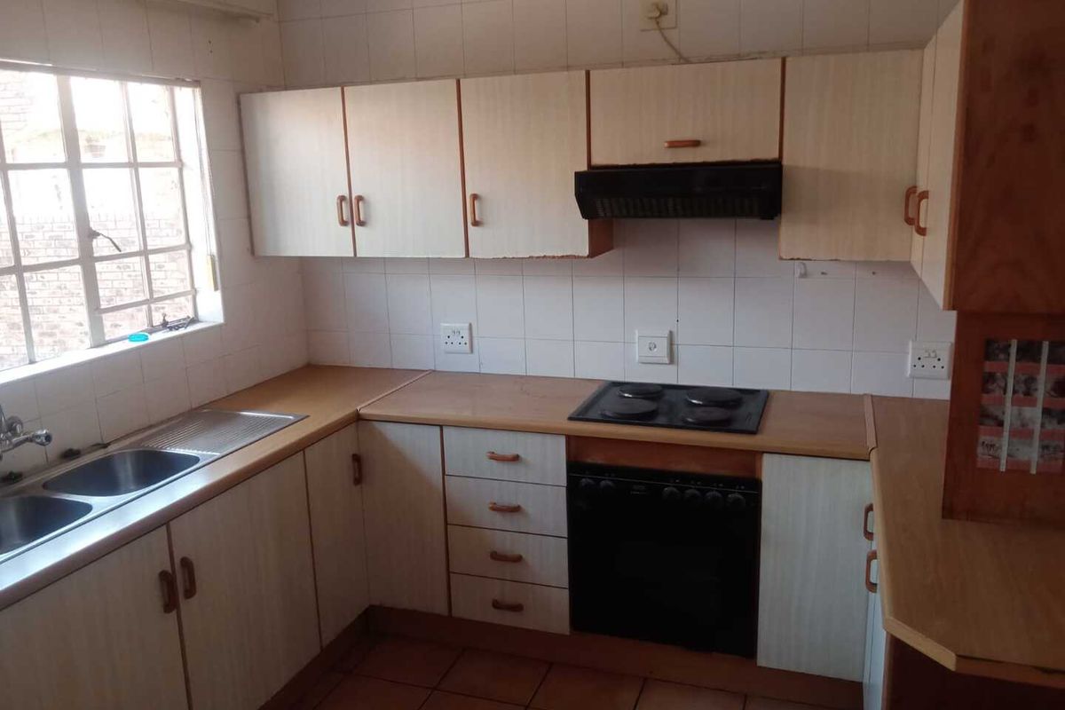 A dated kitchen featuring laminate countertops, built-in cabinetry, a double sink, and an integrated oven with a hob and extractor fan.