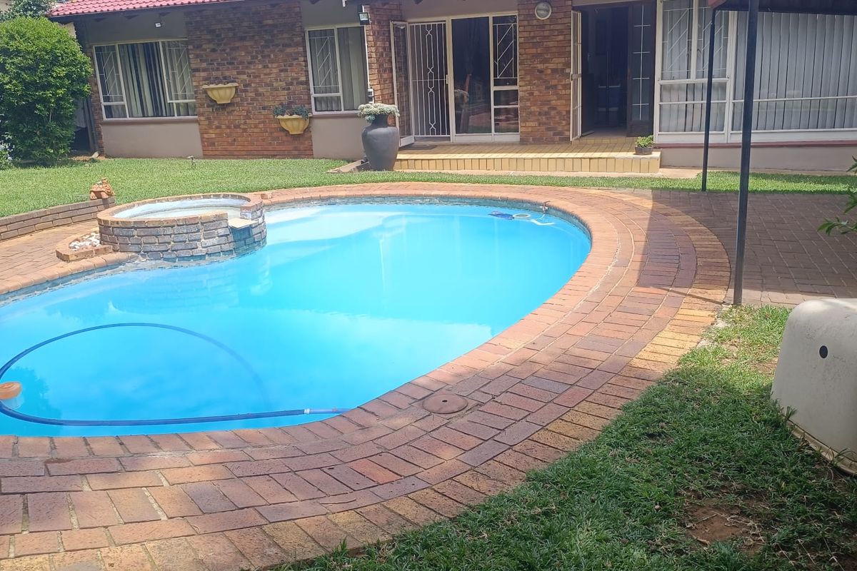 Rear view of the property featuring a swimming pool with a raised brick spa, paved surround, and a red tiled roof with solar water heating.
