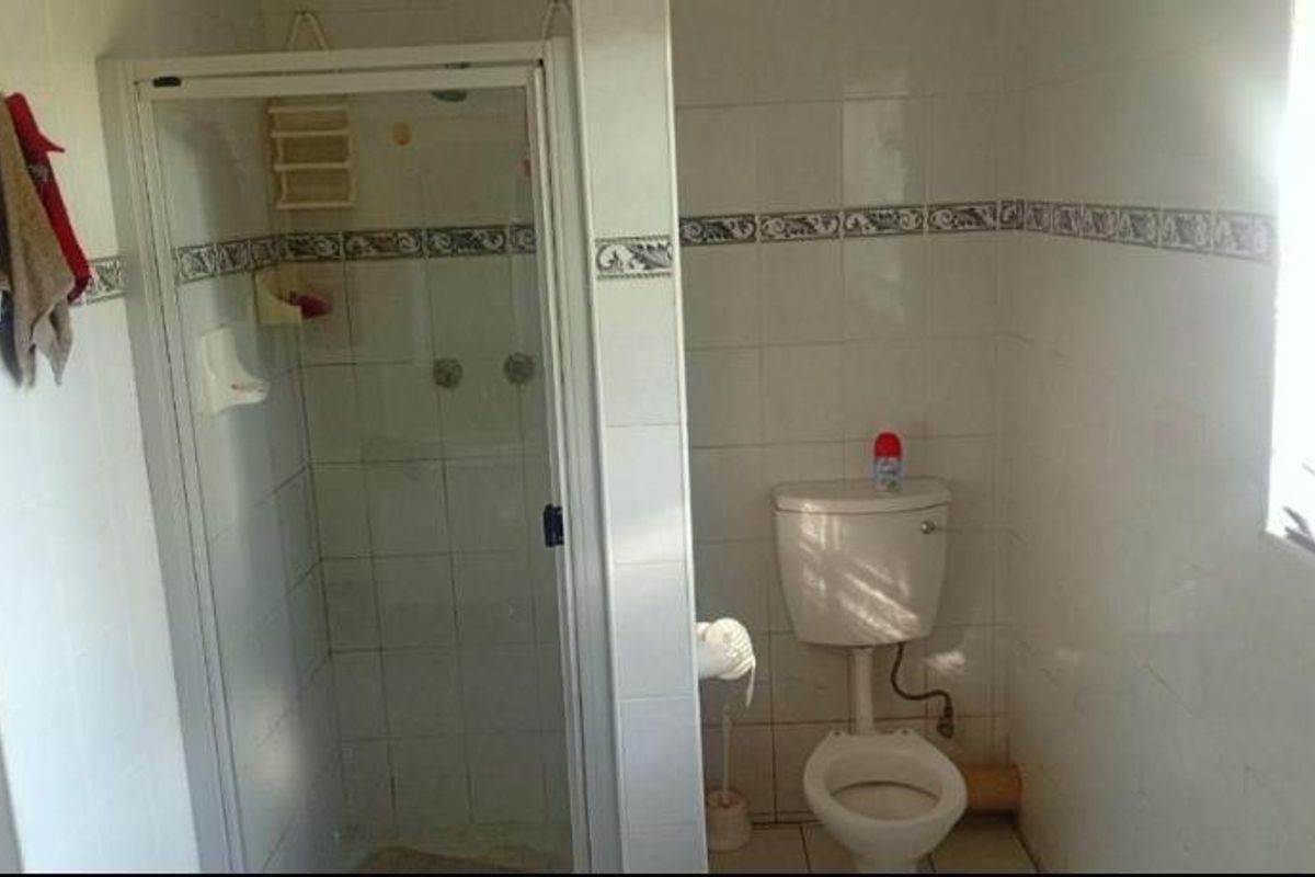 A functional bathroom featuring a glass-enclosed shower and a standard toilet, finished with dated wall tiles.