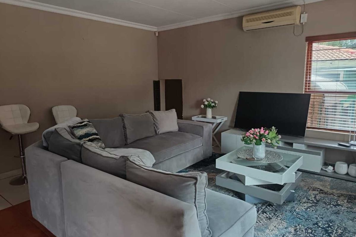 A living room featuring a wall-mounted air conditioning unit, tiled flooring, and a window with blinds, providing a functional living space.