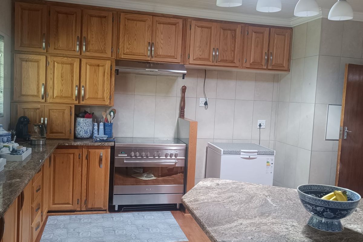 A functional kitchen featuring wood-finish cabinetry, granite countertops, a stainless steel oven with extractor fan, and a central island with breakfast bar seating.