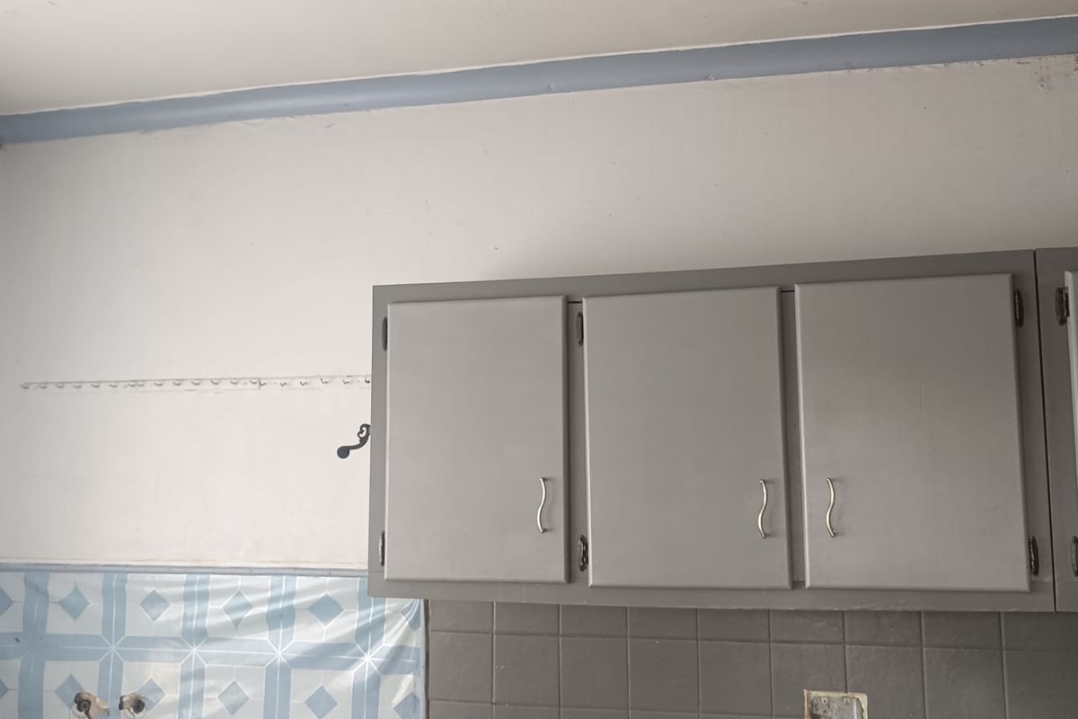 A kitchen area featuring grey wall-mounted cabinetry, a stainless steel sink, and a mix of tiled and unfinished wall surfaces.