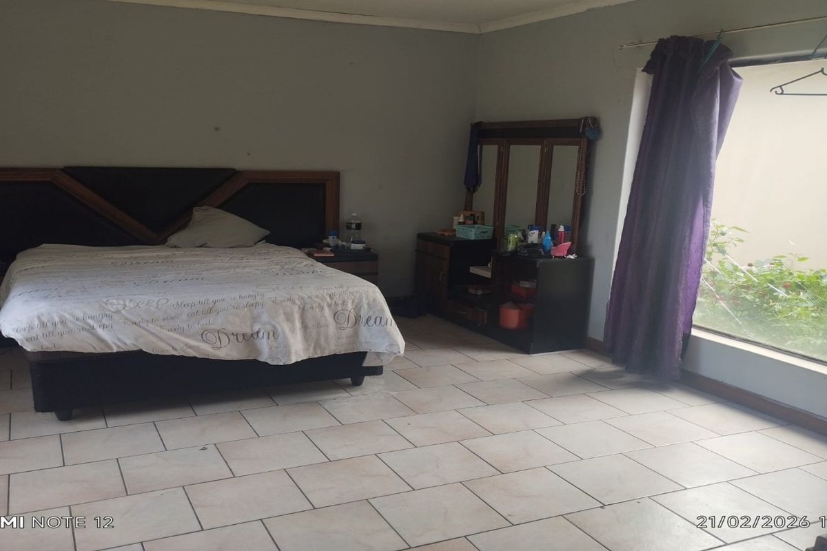 Spacious bedroom featuring large floor tiles and a window overlooking a private garden area.