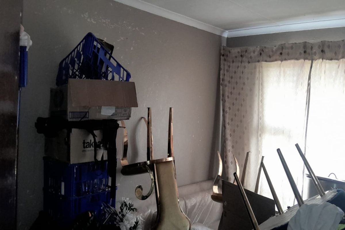 A bedroom space featuring a window with curtains and visible wall surface wear, currently used for storage.