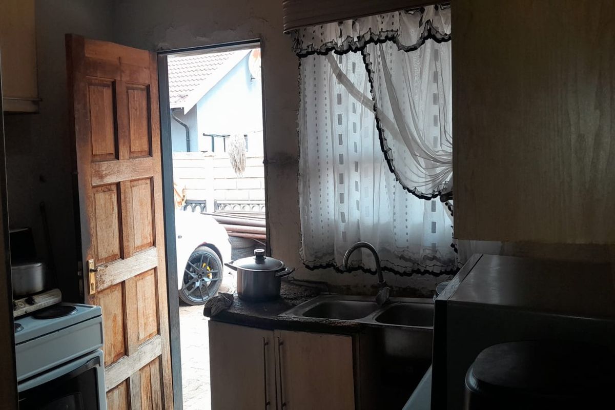 A compact kitchen area featuring a double sink, built-in cabinetry, and direct access to the exterior through a wooden door.