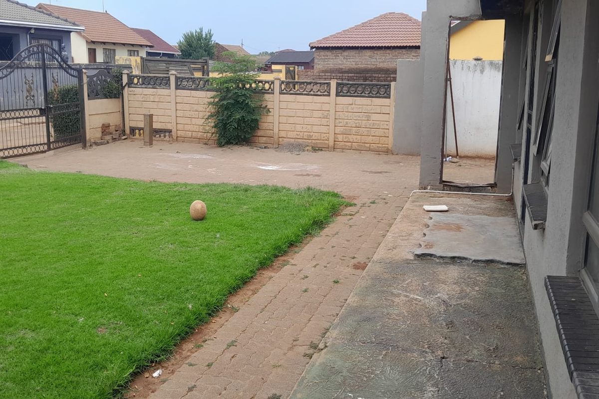 A rear garden area featuring a lawn, paved walkway, and perimeter boundary wall with metal gate access.