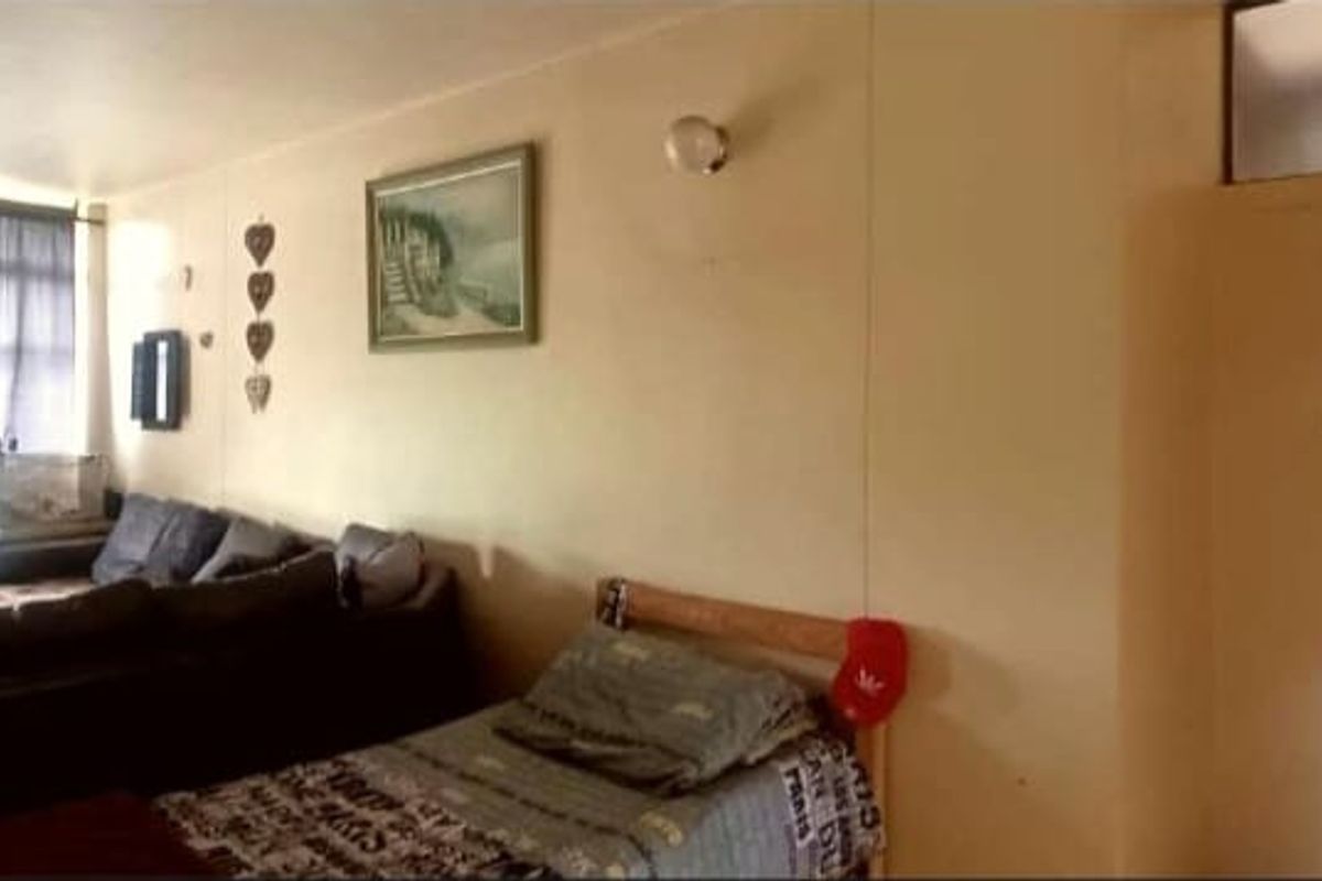 A living area featuring a large window with curtains, neutral wall finishes, and access to an adjacent room through a doorway.