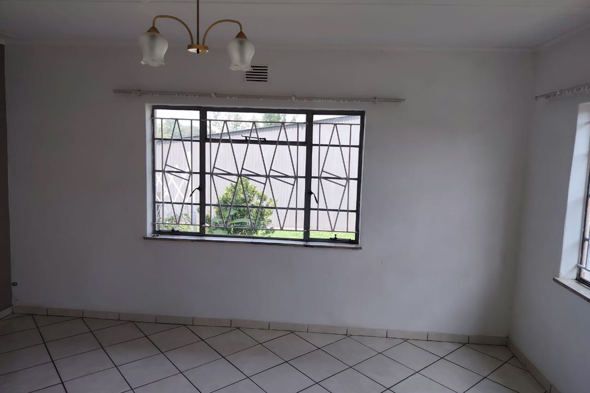 A bright, empty living room featuring tiled flooring, large windows with security bars, and a central ceiling light fixture.