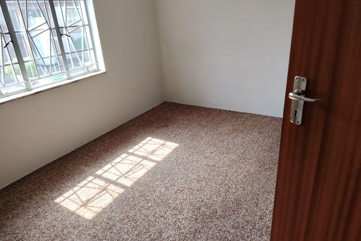 A vacant bedroom featuring neutral walls, carpeted flooring, and a window fitted with security bars.