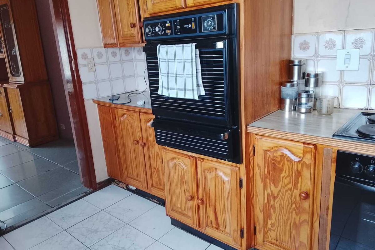 A dated kitchen featuring traditional wood cabinetry, a built-in eye-level oven, and tiled flooring, offering potential for a modern renovation.