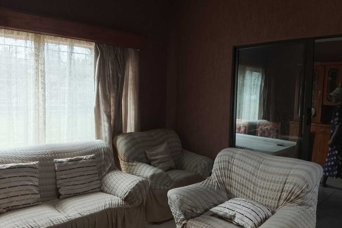 A living room featuring dark textured walls, large windows with curtains, and a sliding door leading to an adjacent space.