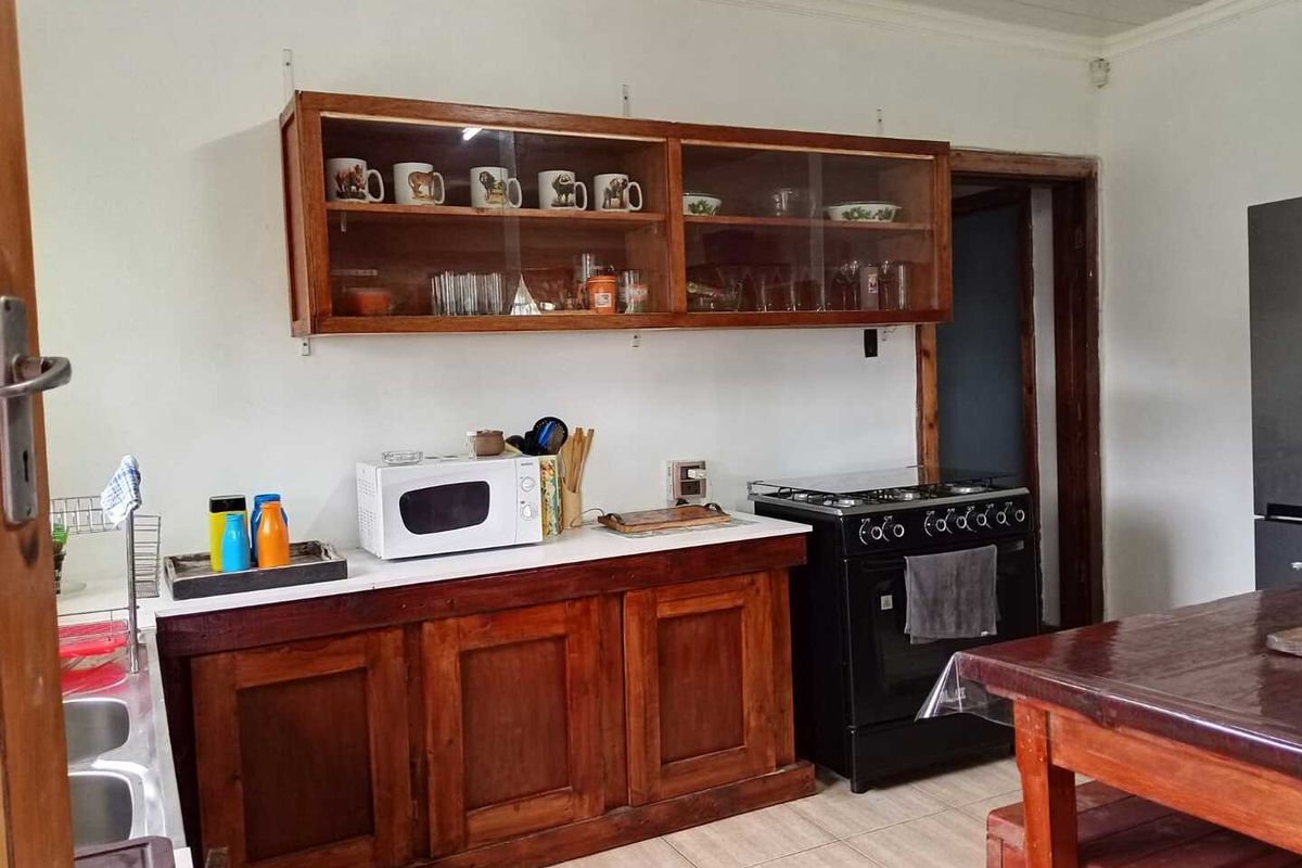 A functional kitchen area featuring wooden cabinetry, a built-in stove, and overhead glass-fronted display cupboards with tiled flooring.