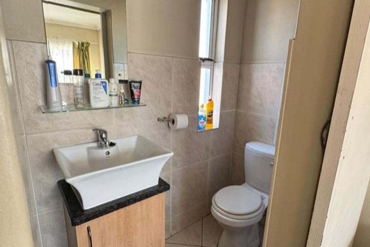 A compact bathroom featuring a modern vessel sink on a wooden vanity, a standard toilet, and neutral wall tiling.