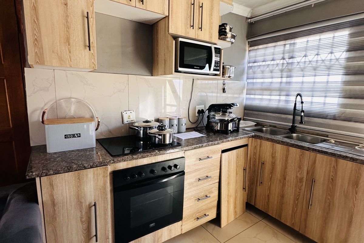 Modern kitchen featuring light wood-grain cabinetry, granite-look countertops, built-in oven, electric hob, and tiled flooring with a window overlooking the exterior.