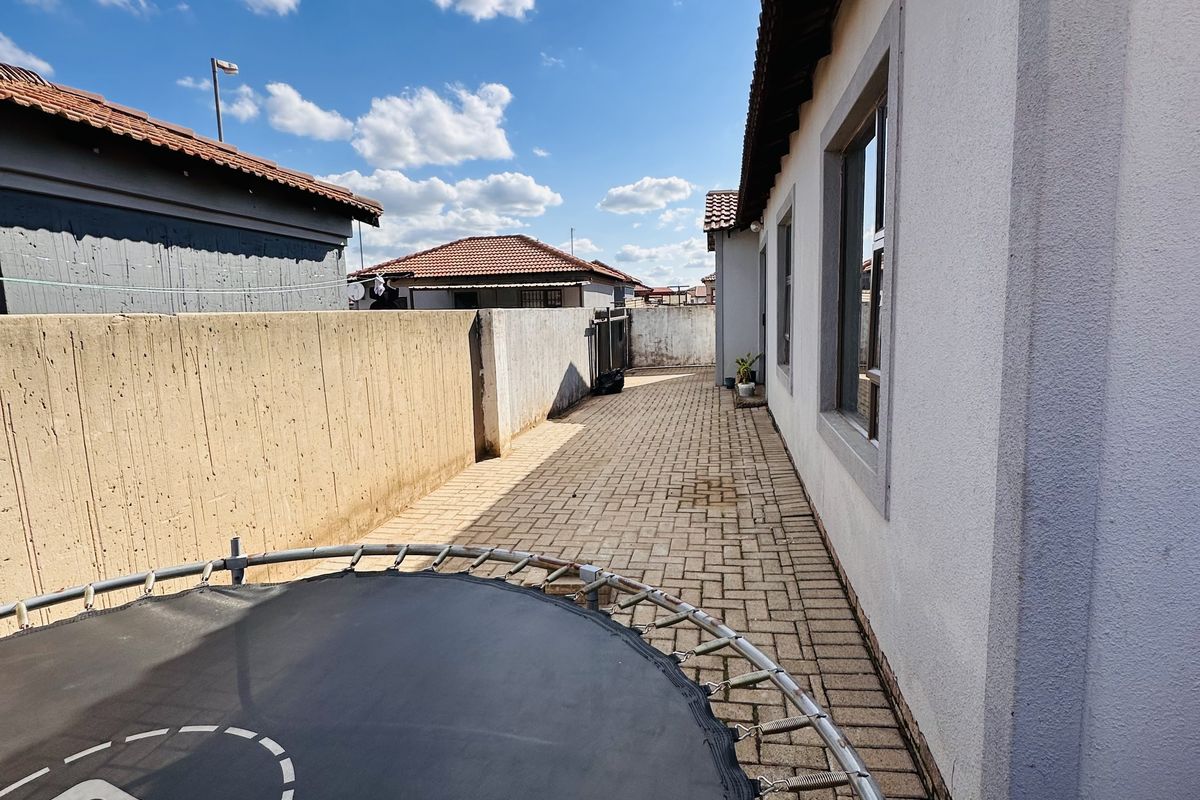 A side exterior walkway featuring paved flooring and a concrete boundary wall, providing access along the side of the house.