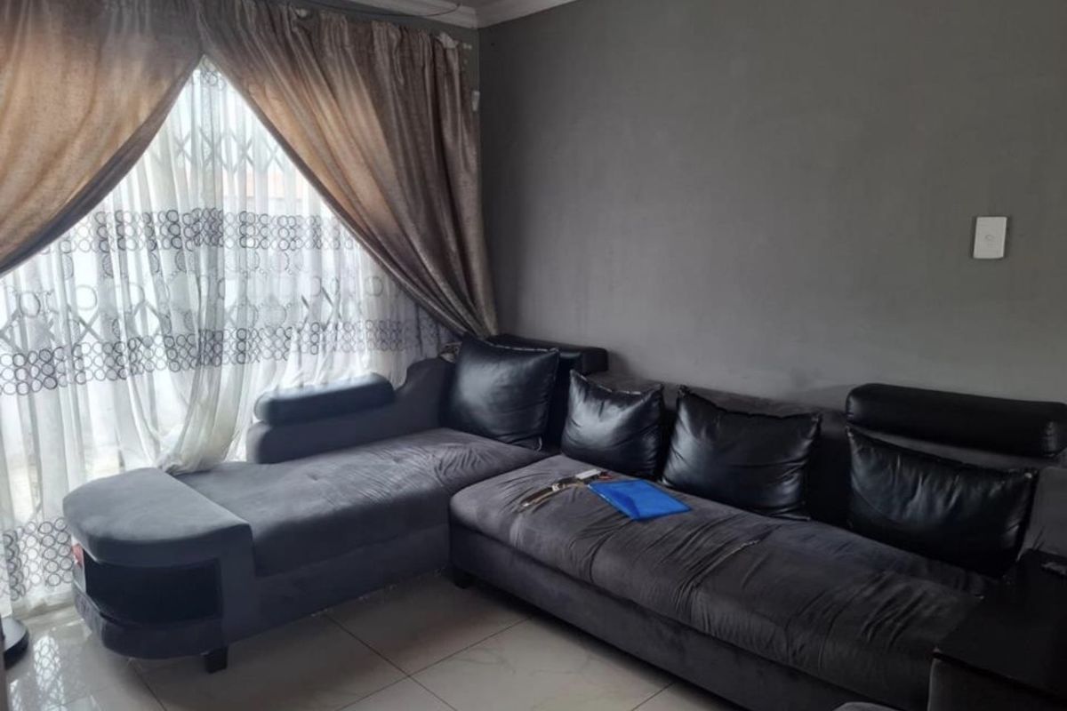 A living room featuring tiled flooring, grey painted walls, and a large window with curtain treatments.