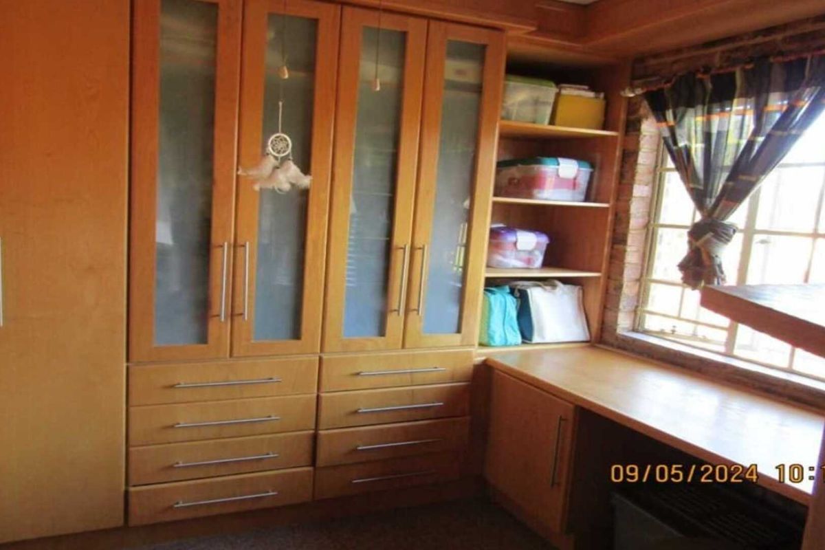 A bedroom featuring extensive built-in wooden cabinetry with glass-panelled doors, integrated drawers, and a dedicated desk area positioned beneath a window.