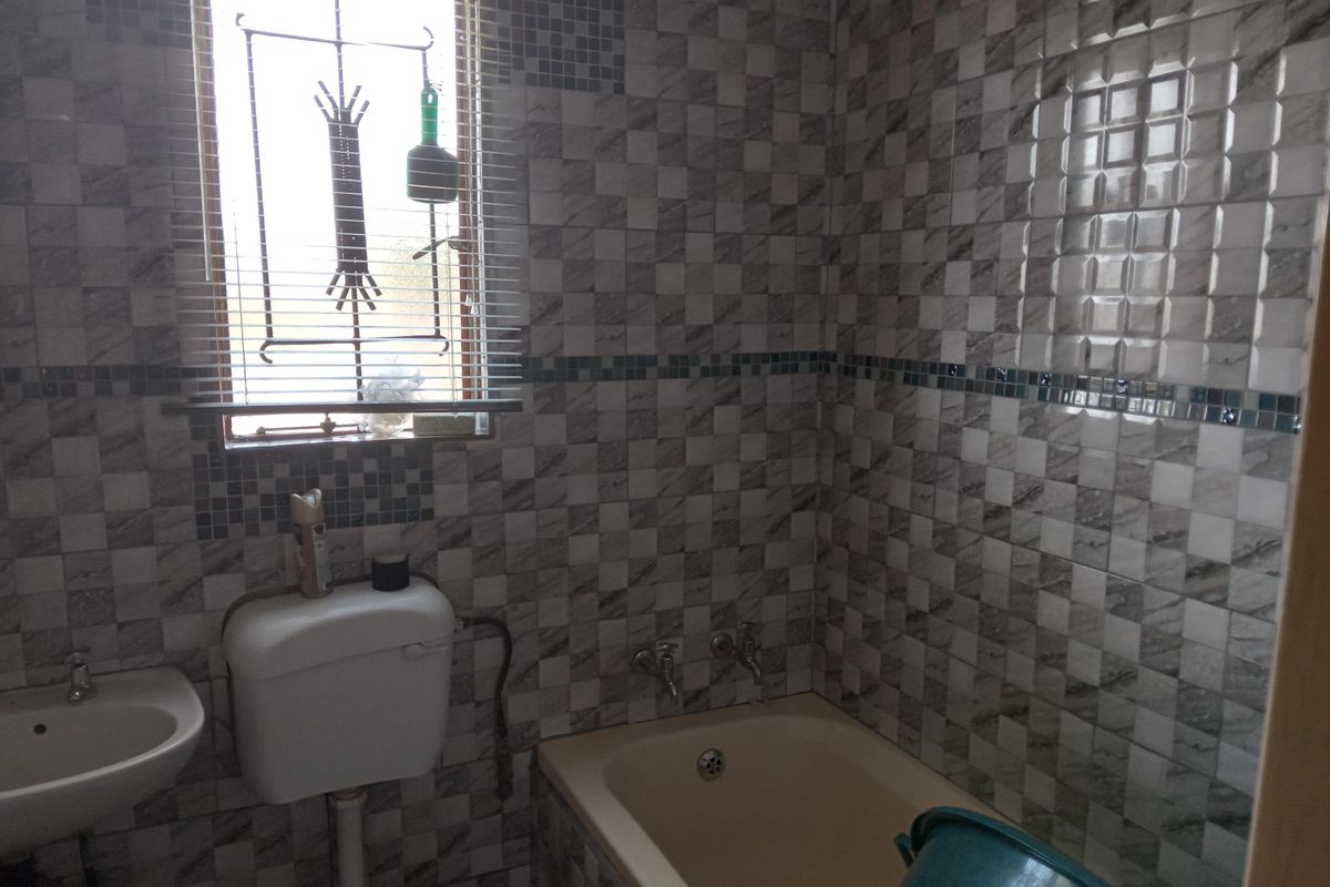 A compact bathroom featuring full-height wall tiling, a standard bathtub, and a wall-mounted basin with security bars on the window.