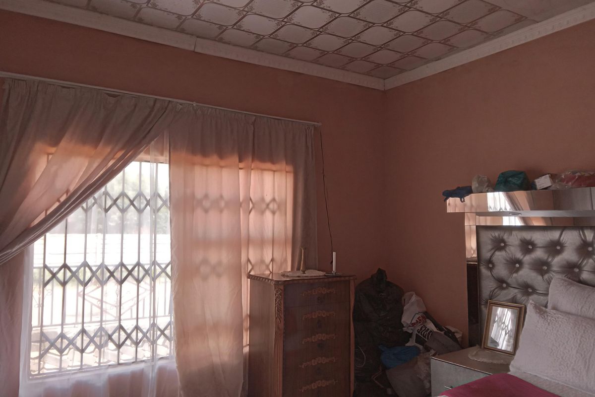 A bedroom featuring a window with security bars, a decorative ceiling, and built-in headboard structure.