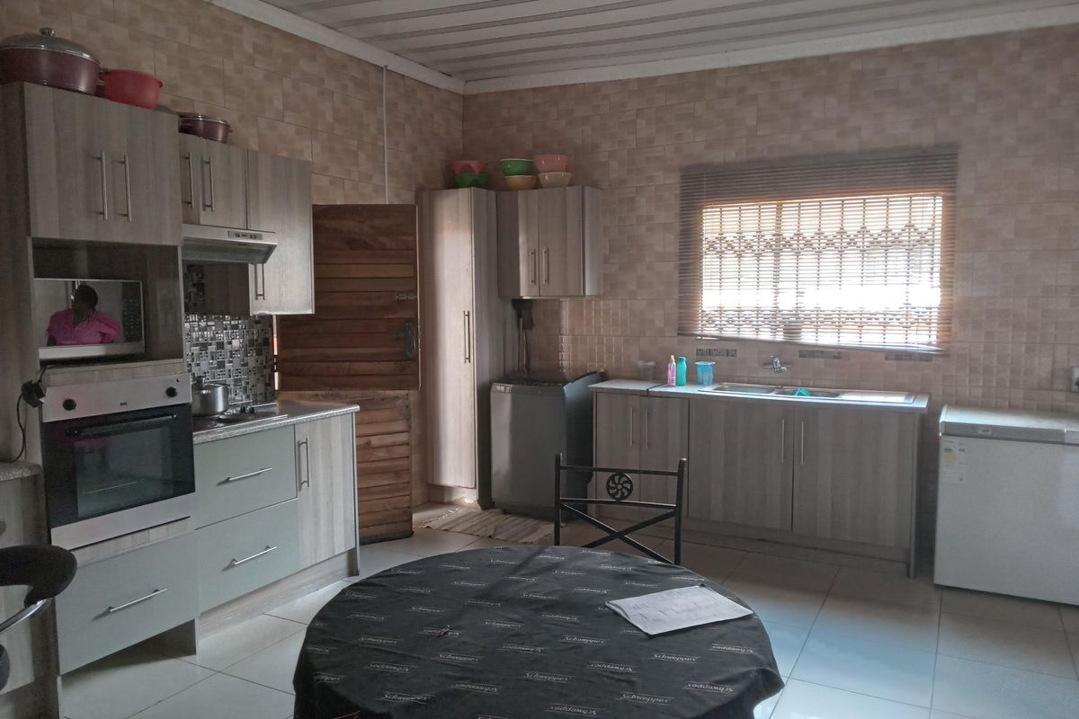 A functional kitchen featuring wood-look cabinetry, built-in oven, extractor fan, and double sink with tiled walls and flooring.