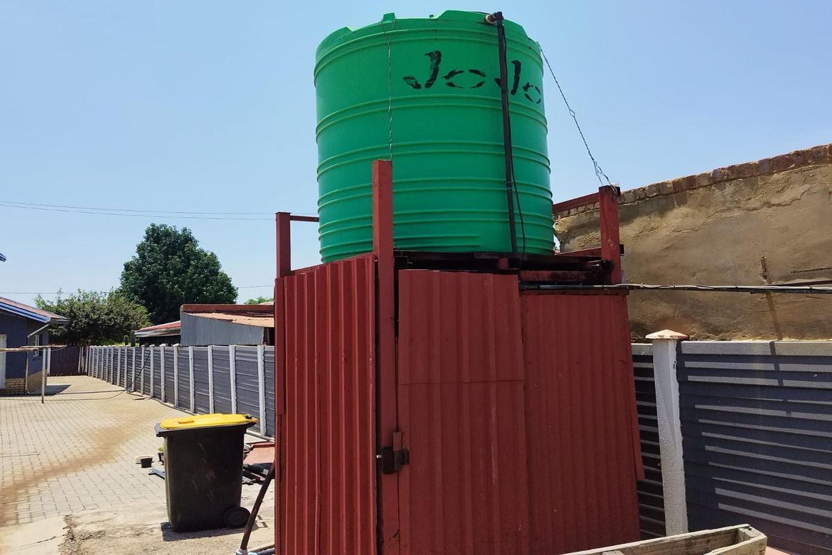 Exterior view of a water storage tank mounted on a corrugated metal support structure located in the rear yard area.