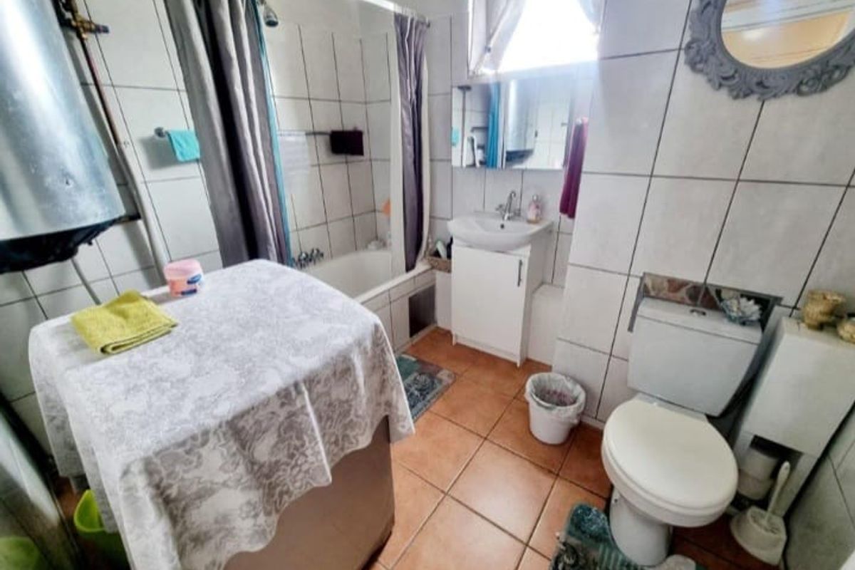 A compact bathroom featuring a bathtub with shower attachment, vanity basin, and toilet, with exposed water heater plumbing.