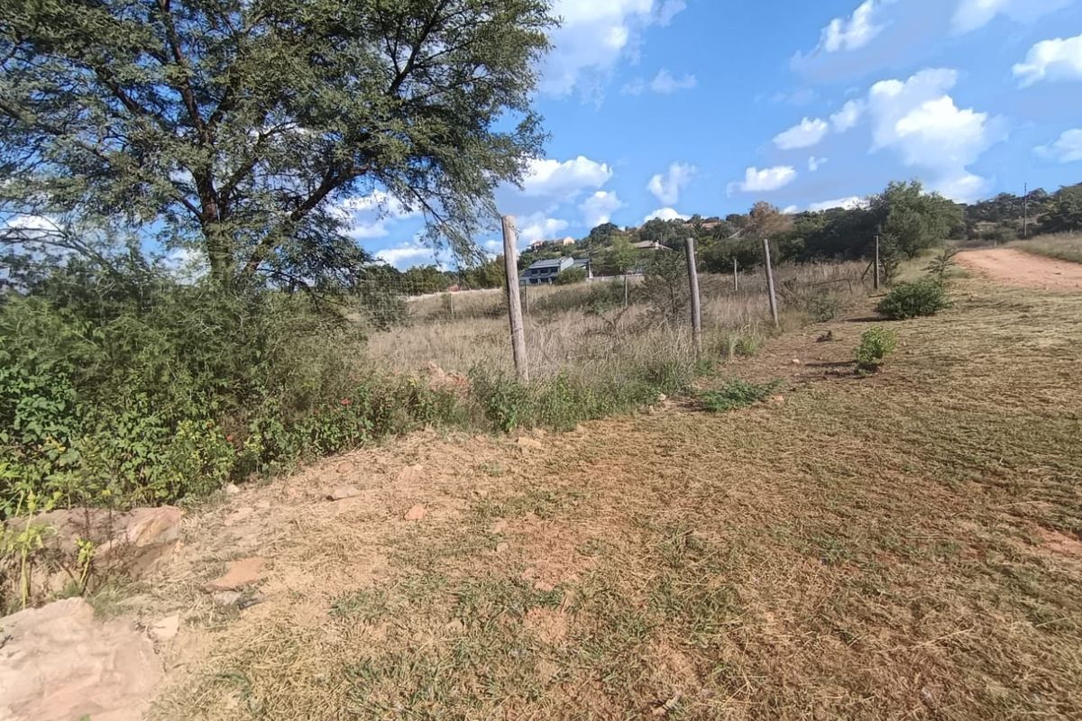 A view of the vacant residential land featuring natural vegetation, mature trees, and existing perimeter wire fencing with wooden posts.