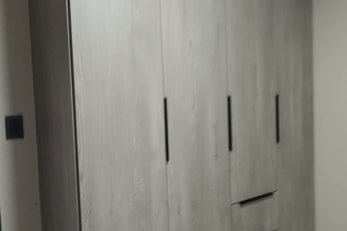 A bedroom featuring modern, light-toned wood grain built-in cabinetry with sleek black handles and integrated drawers.