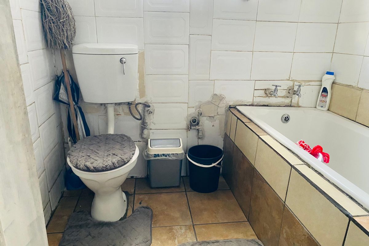 A dated bathroom featuring a standard bathtub and toilet, currently requiring significant maintenance and cosmetic updates to the wall tiling and plumbing fixtures.