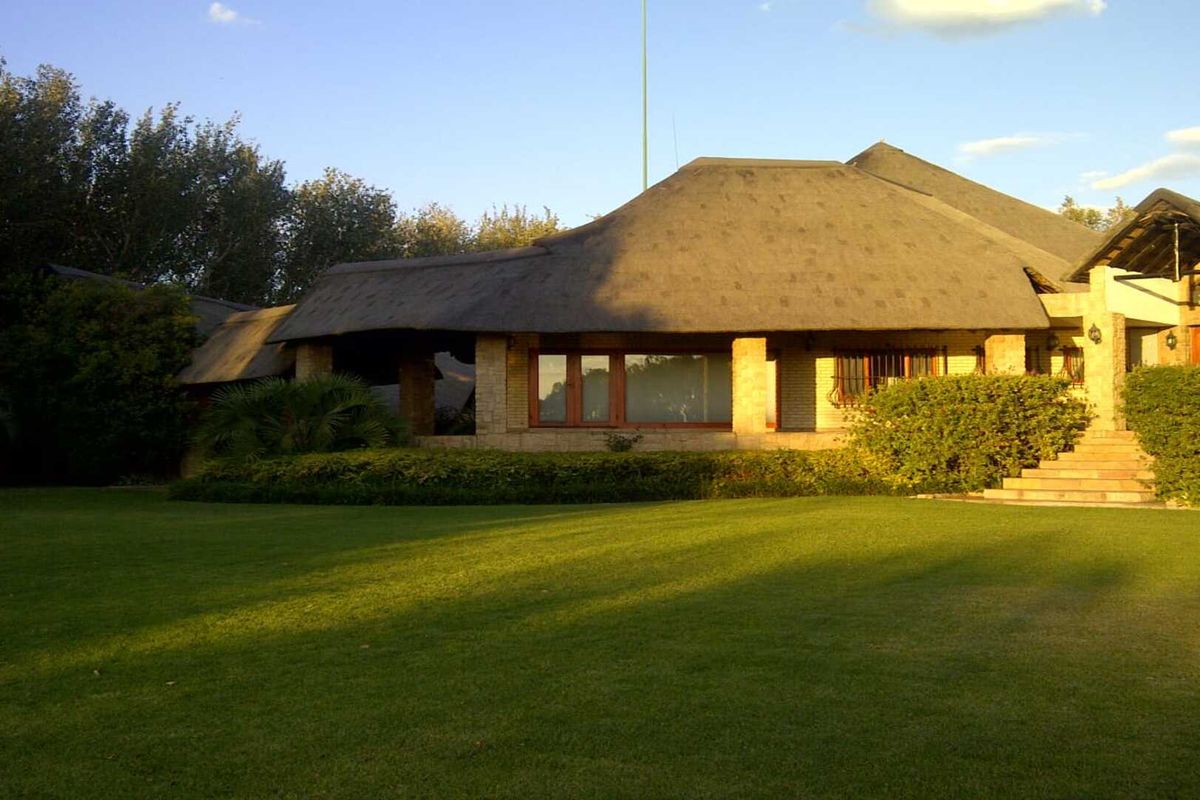 A view of the rear elevation of a house featuring a traditional thatched roof, brick facade, and a spacious, well-maintained lawn.
