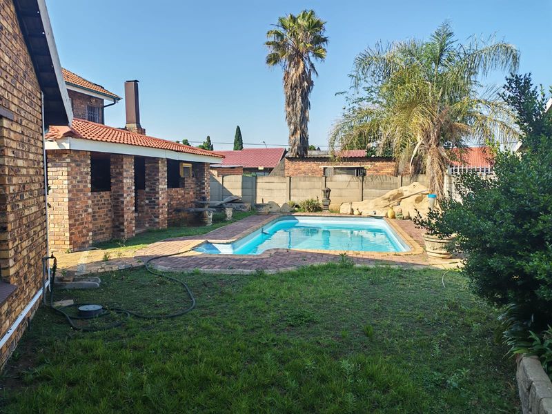Rear garden area featuring a swimming pool, paved surround, and a covered brick patio structure.