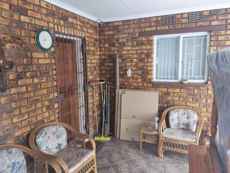 A covered patio area featuring exposed face-brick walls, tiled flooring, and a security gate, providing a functional outdoor living space.