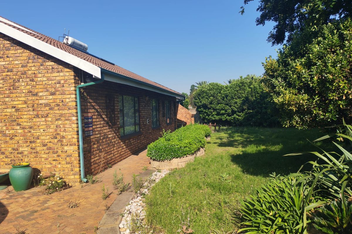 A side view of the brick house exterior featuring a paved walkway, established garden beds, and a solar water heating system on the roof.
