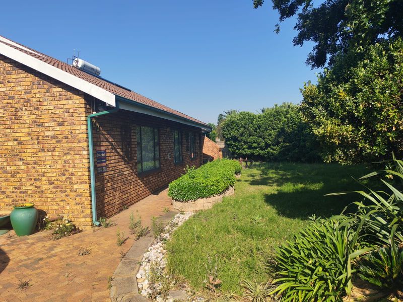 A side view of the brick house exterior featuring a paved walkway, established garden beds, and a solar water heating system on the roof.