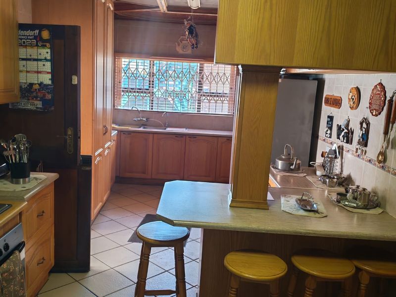 A traditional kitchen featuring wood-toned cabinetry, a breakfast bar, tiled flooring, and a built-in extractor hood over the cooking area.