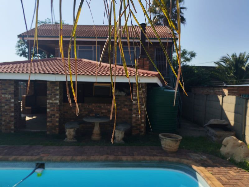 Rear view of a double-story brick house featuring a covered patio area, swimming pool, and a large water storage tank.