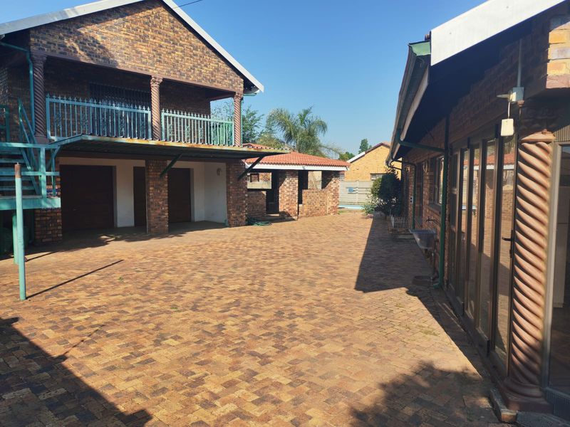 Spacious paved courtyard area featuring brick construction, a covered balcony, and access to the main dwelling and outdoor entertainment structures.