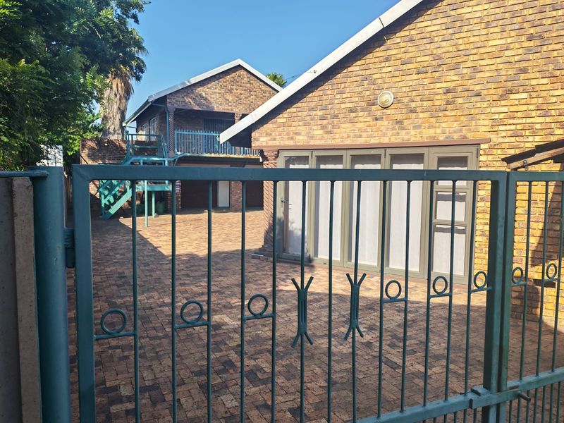 A paved courtyard area featuring a face-brick exterior, a metal staircase leading to an upper level, and a secure gated entrance.