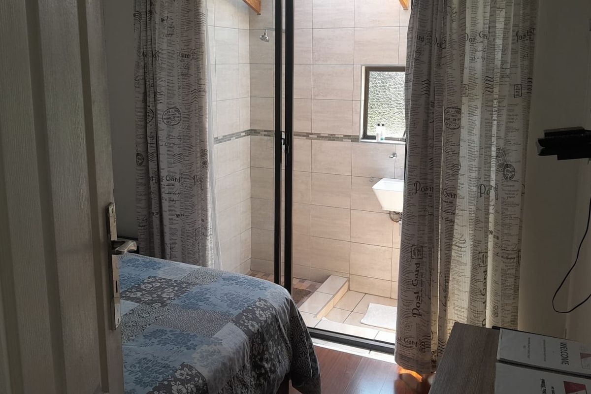 A bedroom featuring an integrated en-suite bathroom with tiled walls, a shower, and a wall-mounted basin.