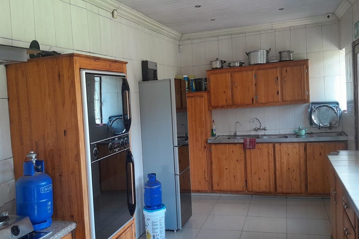 A functional kitchen featuring wooden cabinetry, built-in oven, double sink, and tiled flooring, offering a practical layout for daily meal preparation.