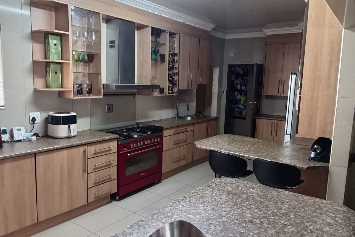 A functional kitchen featuring light wood cabinetry, granite-style countertops, a red freestanding gas stove with extractor fan, and a breakfast bar island.