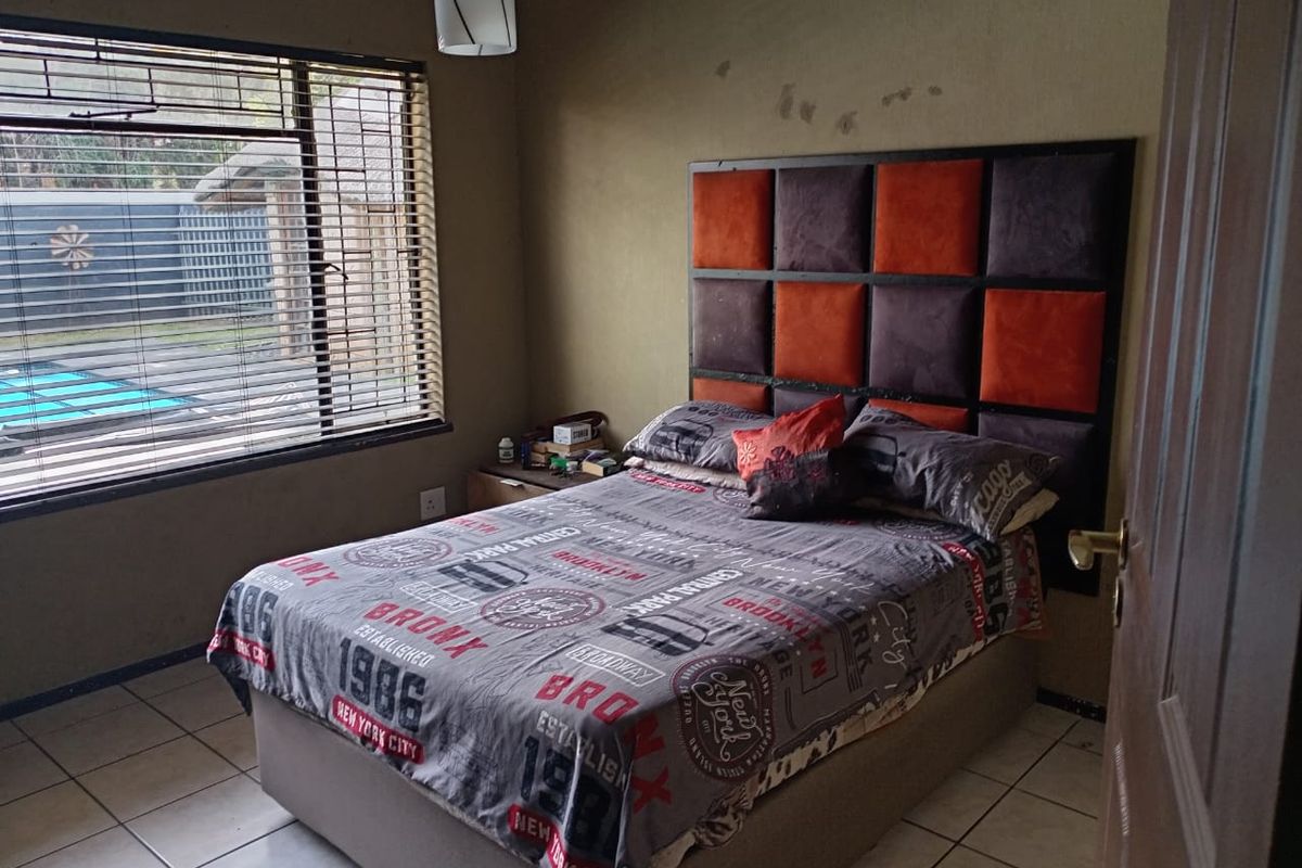 A bedroom featuring tiled flooring, a large window with blinds, and a built-in headboard, overlooking the outdoor pool area.