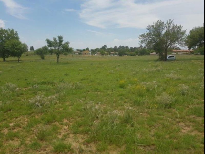 A wide-angle view of a vacant residential plot featuring natural grass, scattered trees, and a level landscape suitable for future development.