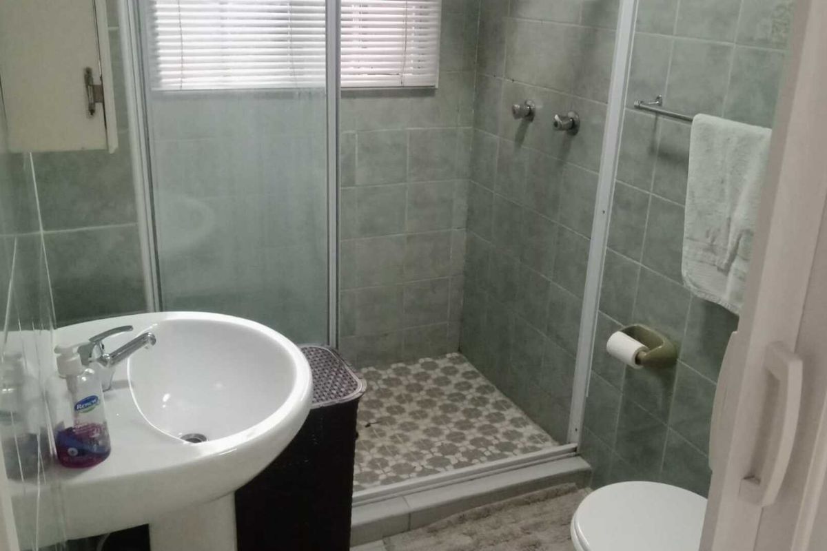A functional bathroom featuring a pedestal basin, a tiled shower enclosure with a glass door, and a standard toilet.