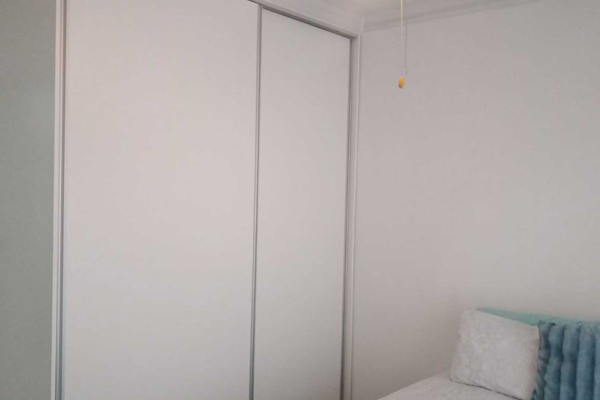 A bedroom featuring built-in sliding door cupboards with a clean, minimalist white finish.