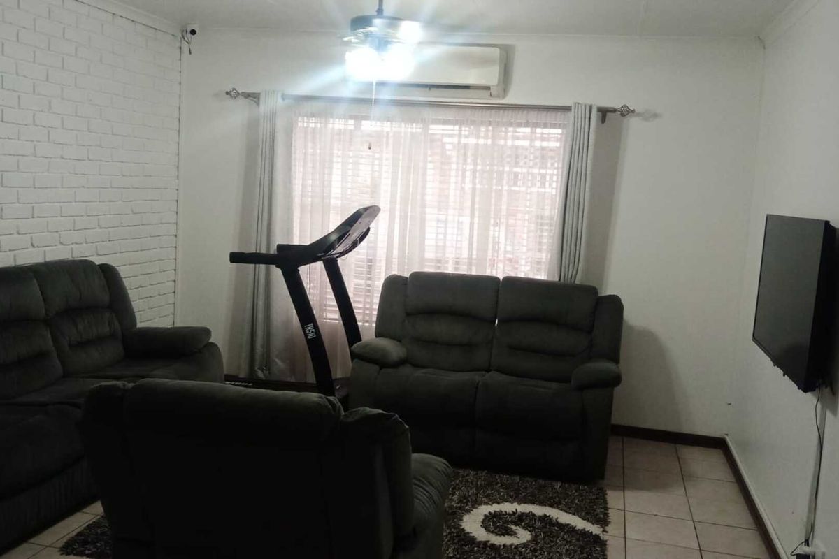 A living room featuring a white painted brick feature wall, tiled flooring, and a wall-mounted air conditioning unit.