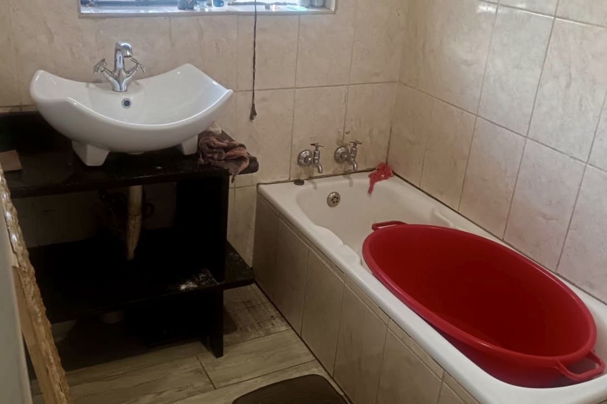 A functional bathroom featuring a tiled bathtub, a vessel sink vanity, and a window with security bars.