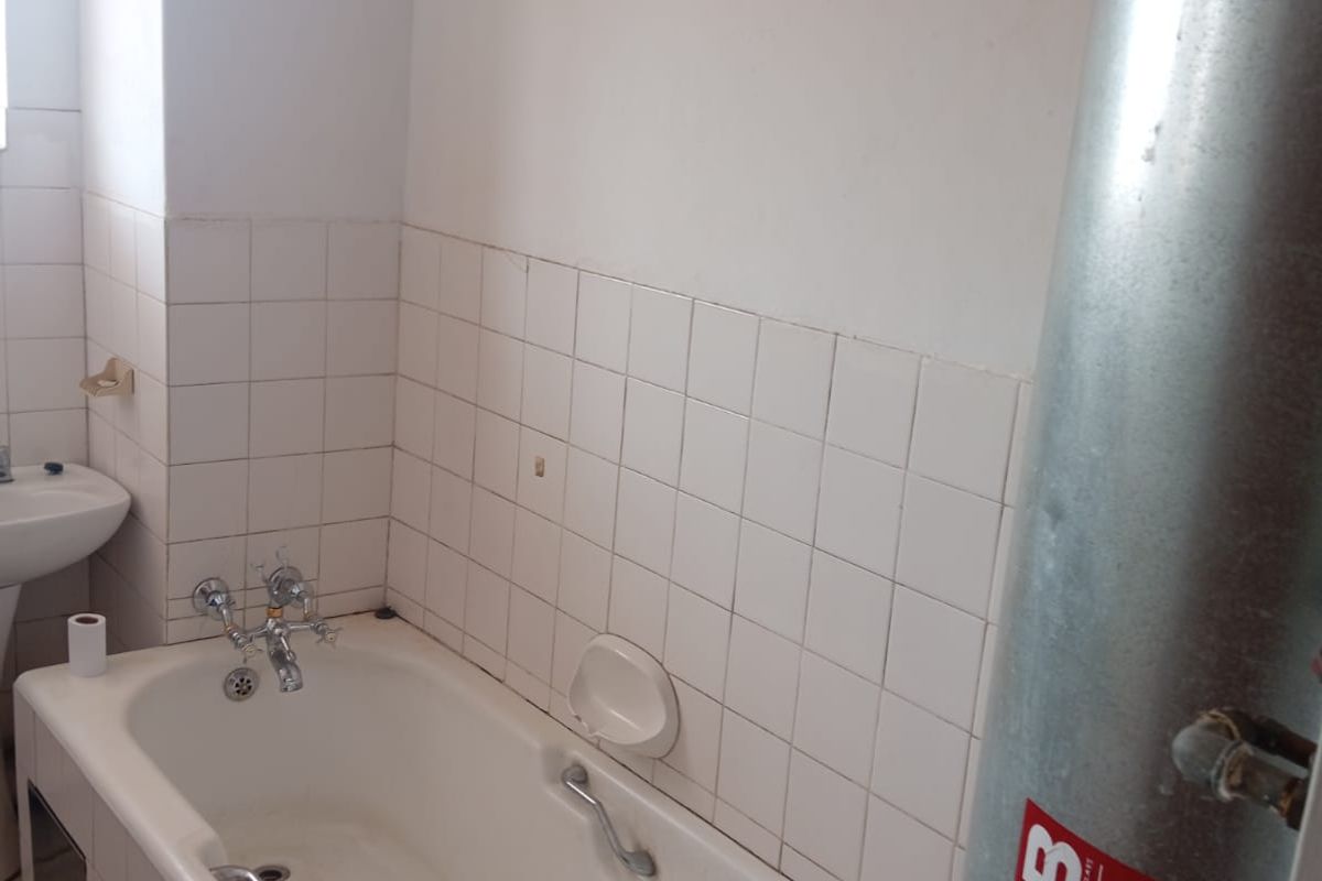 A functional bathroom featuring a standard bathtub with tiled surround and an exposed wall-mounted water heater unit.
