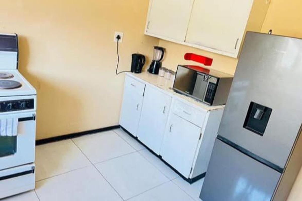 A functional kitchen area featuring white cabinetry, tiled flooring, and space for a freestanding stove and refrigerator.