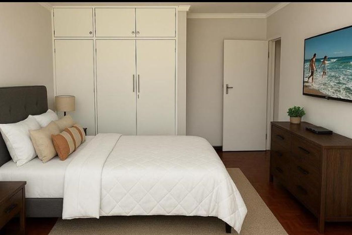 A well-maintained bedroom featuring built-in floor-to-ceiling cabinetry, polished timber flooring, and neutral wall finishes.